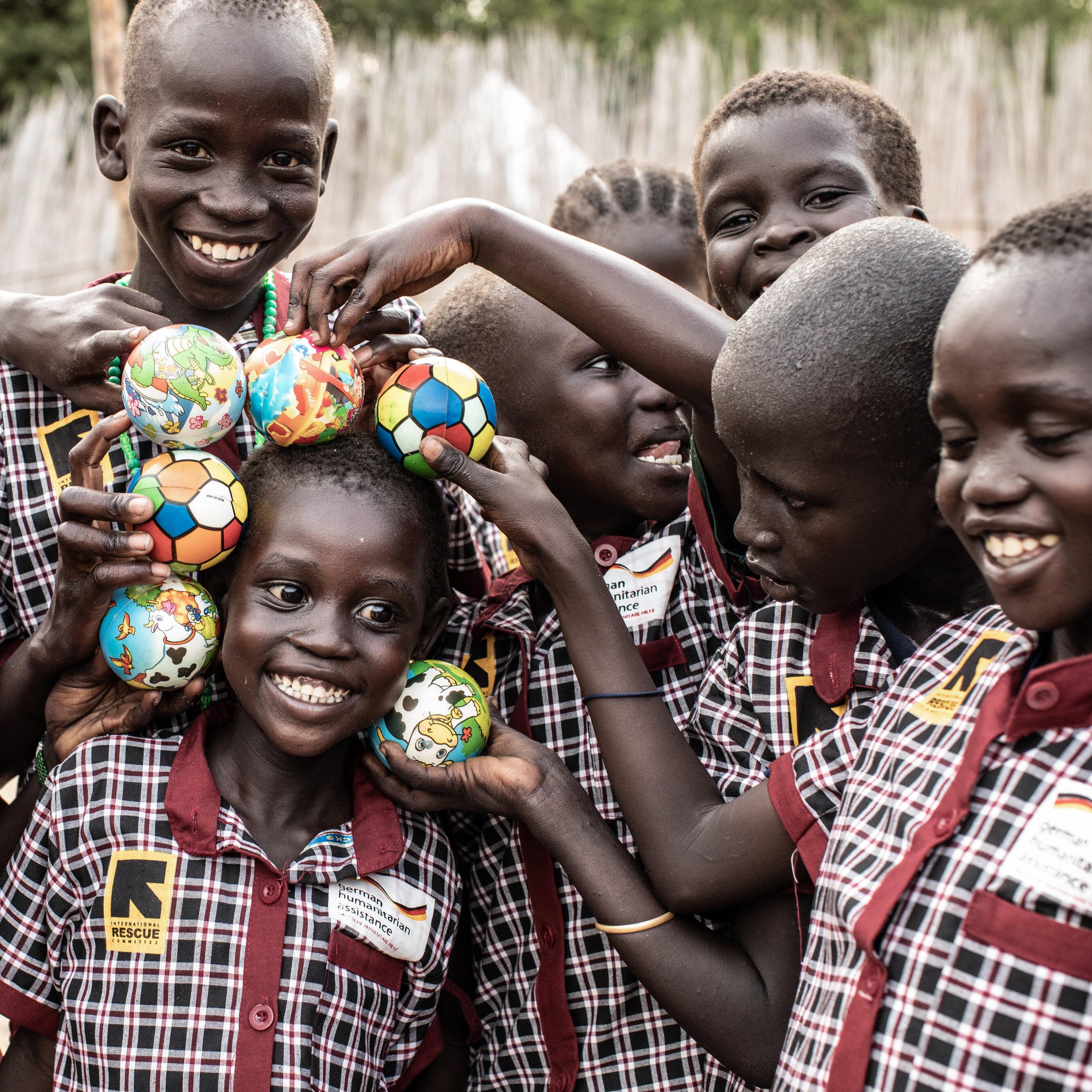 A group of children smile together, playing in the yard of the IRC Child-Friendly Learning Center in Sudan